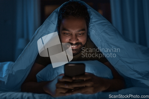 Image of indian man with smartphone in bed at home at night