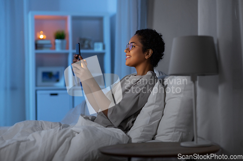 Image of african woman with smartphone in bed at night