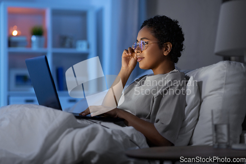 Image of woman with laptop in bed at home at night