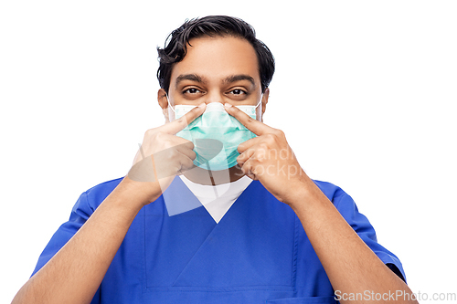 Image of indian male doctor in blue uniform putting mask on