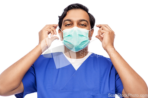 Image of indian male doctor in blue uniform putting mask on