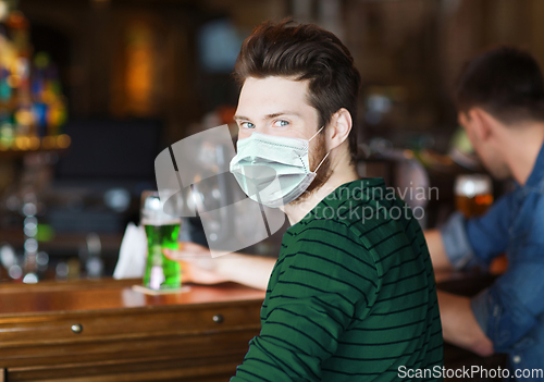 Image of young man in mask drinking green beer at bar