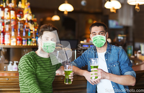 Image of male friends in masks drinking green beer at bar