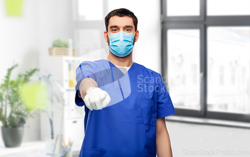 Image of male doctor in blue scrubs and mask points finger