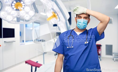 Image of tired male doctor in blue uniform, mask and gloves