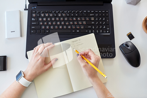 Image of woman writing working plan to notebook at office