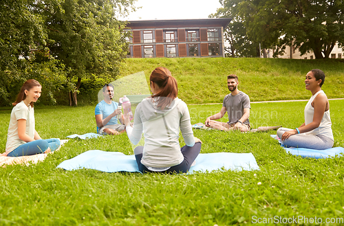 Image of group of people sitting on yoga mats at park