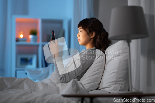 Image of asian woman with smartphone in bed at night