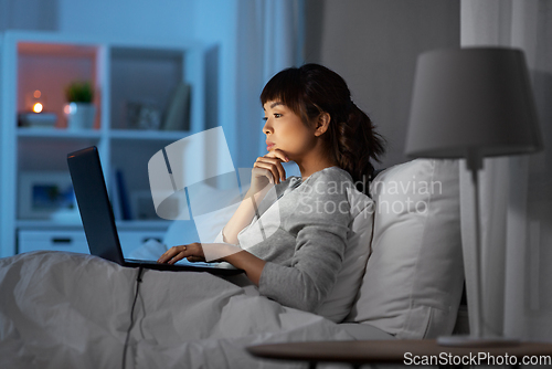 Image of woman with laptop in bed at home at night