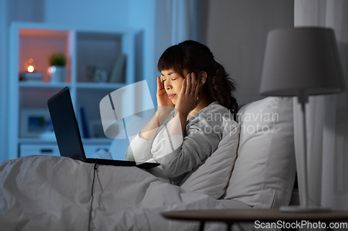 Image of stressed woman with laptop working in bed at night