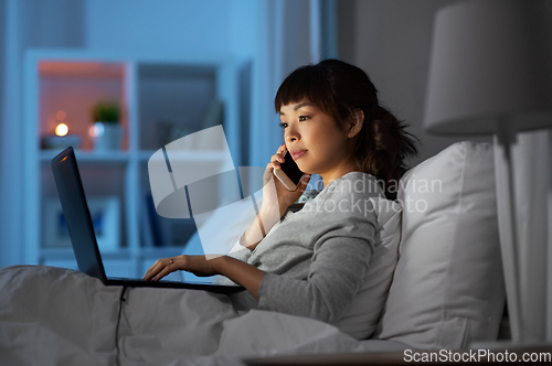 Image of woman with laptop calling on phone in bed at night