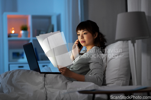 Image of woman with laptop calling on phone in bed at night