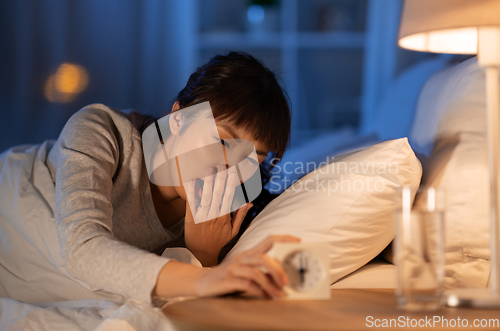 Image of asian woman with clock yawning in bed at night