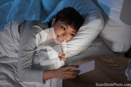 Image of asian woman with smartphone in bed at night