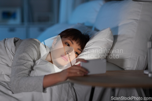 Image of asian woman with smartphone in bed at night