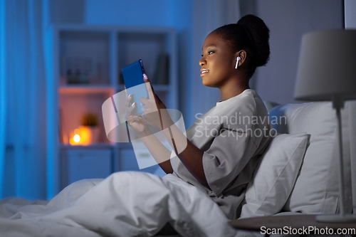 Image of woman with tablet pc and earphones in bed at night