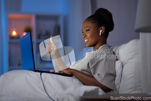 Image of woman with laptop and earphones in bed at night