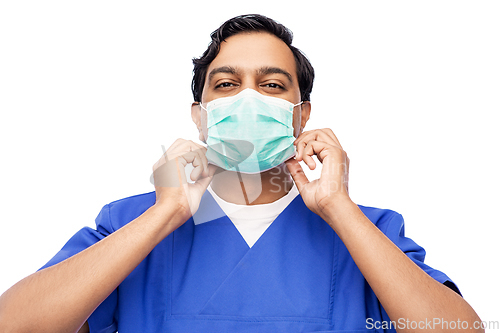 Image of indian male doctor in blue uniform putting mask on