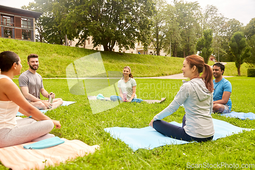 Image of group of people sitting on yoga mats at park