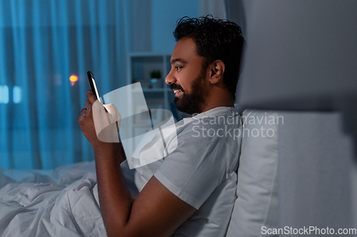 Image of indian man with smartphone in bed at home at night