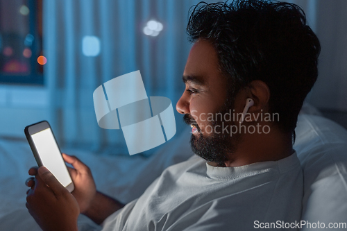 Image of man with smartphone and earphones in bed at night