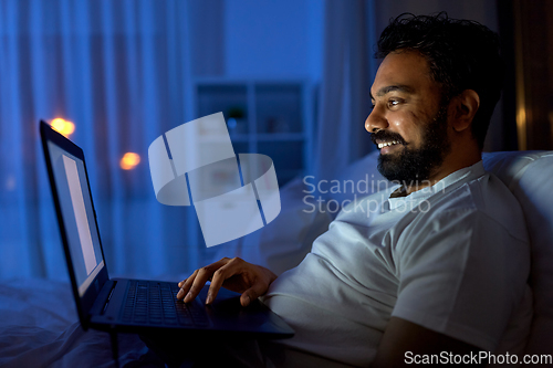 Image of indian man with laptop in bed at home at night