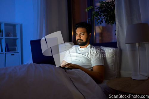 Image of indian man with laptop in bed at home at night