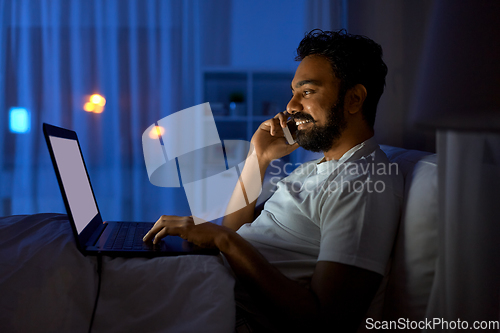 Image of indian man with laptop calling on phone at night