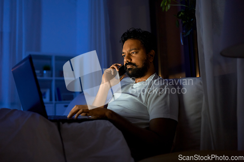 Image of indian man with laptop calling on phone at night