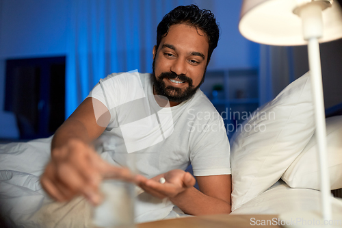 Image of indian man with medicine and water in bed at night