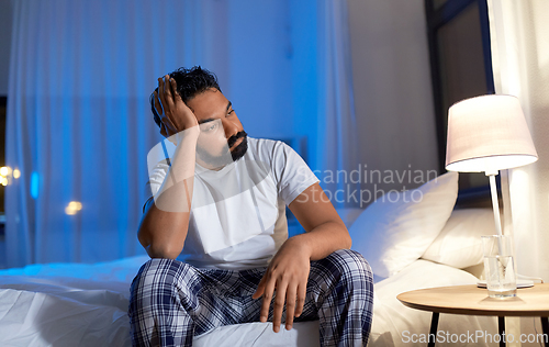 Image of stressed indian man sitting on bed at night