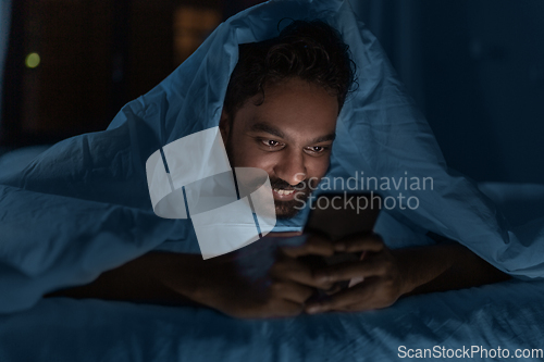 Image of indian man with smartphone in bed at home at night