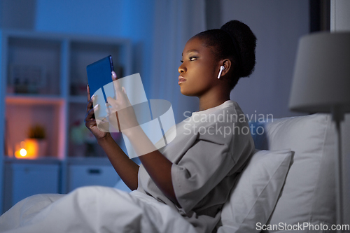 Image of woman with tablet pc and earphones in bed at night