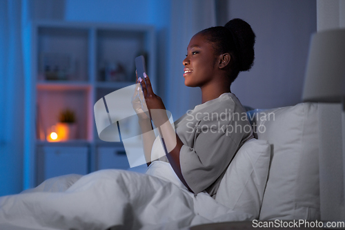 Image of woman with smartphone in bed at home at night