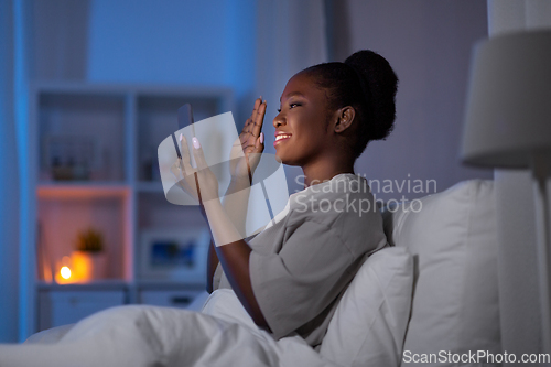 Image of woman with smartphone and earbuds in bed at night