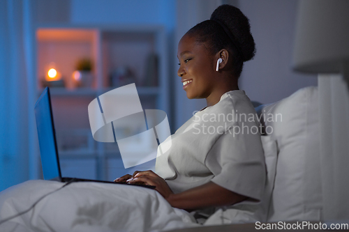 Image of woman with laptop and earphones in bed at night