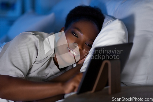 Image of woman with tablet pc in bed at home at night