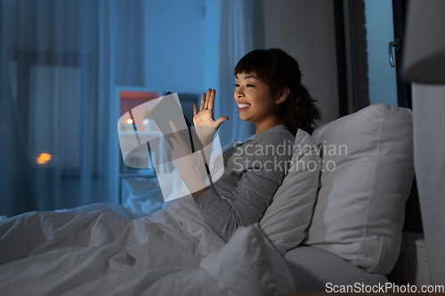 Image of woman with tablet pc in bed has video call at night