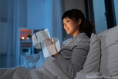 Image of asian woman with smartphone in bed at night