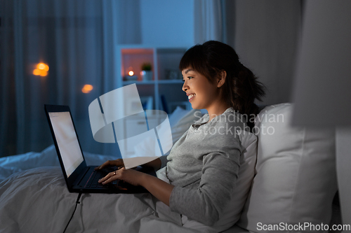 Image of woman with laptop in bed at home at night