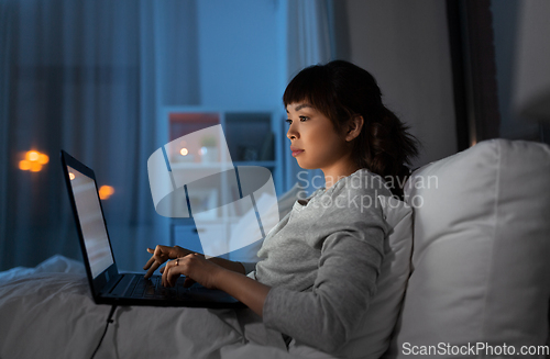 Image of woman with laptop in bed at home at night