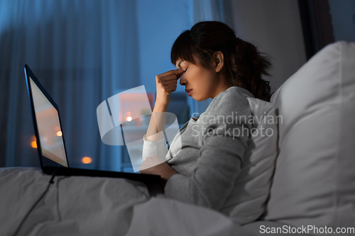 Image of stressed woman with laptop working in bed at night