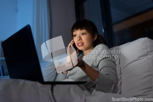 Image of woman with laptop calling on phone in bed at night