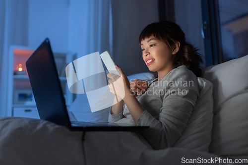 Image of asian woman with smartphone in bed at night