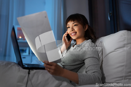 Image of woman with laptop calling on phone in bed at night