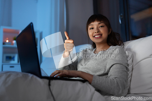 Image of woman with laptop in bed at night shows thumbs up