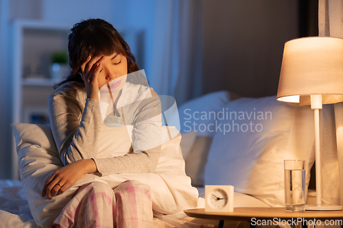 Image of stressed asian woman sitting on bed at night