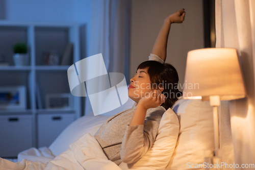 Image of tired asian woman stretching in bed at night