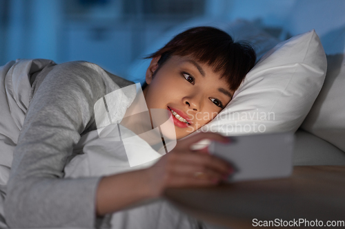 Image of asian woman with smartphone in bed at night