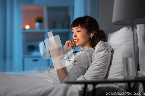 Image of woman with phone and earphones in bed at night